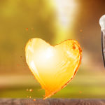 Beer in glass and splash in shape of heart on wooden table with
